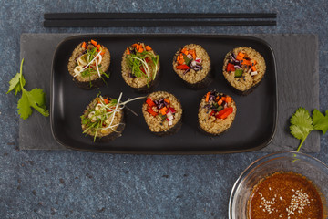 Vegan sushi rolls with quinoa, vegetables and soy-nut sauce on a black plate, black background. Top view. Vegan Healthy Food Concept.
