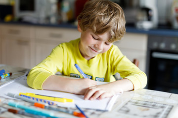 Tired kid boy at home making homework writing letters with colorful pens