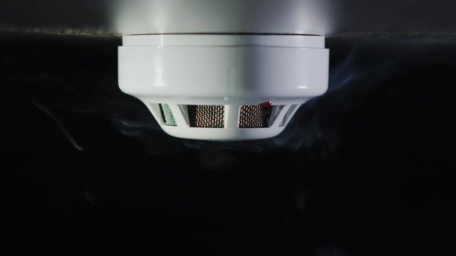 Smoke detector on a black background. There are trickles of smoke. The sensor is triggered - the red alarm indicator lights up