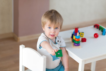 2 year-old child playing with educational cup toys at home. Little blond baby boy with blue eyes is...