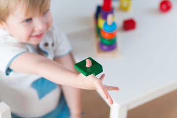 2 year-old child playing with educational cup toys at home. Little blond baby boy with blue eyes is playing with pyramid toy on the floor. Little kid have fun indoors