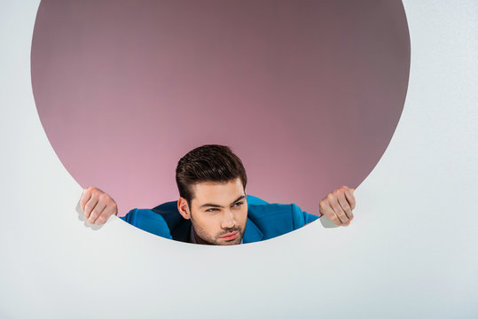 stylish bearded young man looking through hole on grey