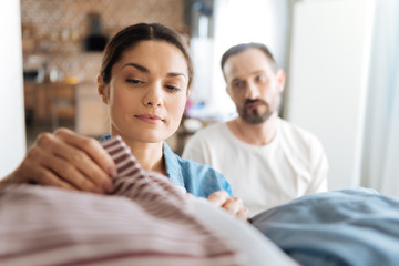 After laundry. Attractive pretty concentrated woman touching clothes while thinking and looking down