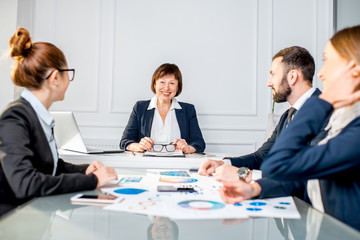 Portrait of a senior businesswoman sitting during the conference with young colleagues in the office