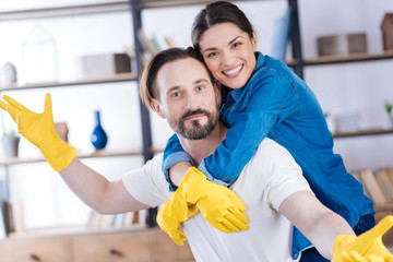 Spring cleaning. Energetic enthusiastic young couple looking at the camera while wearing gloves and wife hugging husband