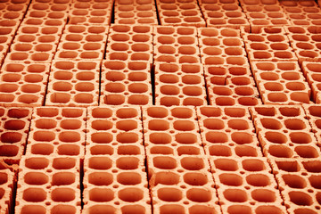 Pile of red hollow bricks with large holes forming lines in repeating geometric pattern similar to honeycomb background. Photo perspective from above.