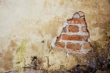 Old dirty and grungy plastered wall facade of an abandoned house with a hole showing the underlying red bricks below the cement.