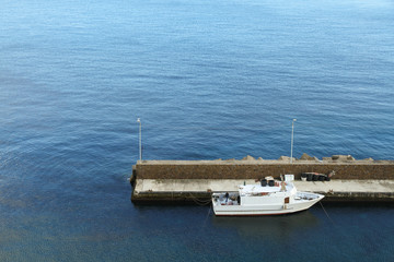 Harbour and small white fishing boat tied to the pier in the Mediterranean Sea with blue sea waters on the background. Photo perspective from above.