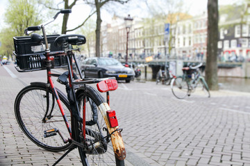 Bicycle parked on the street in the foreground with a typical canal and architecture of Amsterdam, Netherlands slightly out focus on the background during Spring time in the Dutch capital.