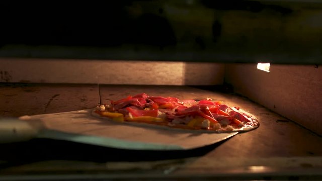 Shovel putting pizza into oven. Thin crust, vegetables and meat.