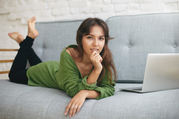 Obraz premium Pretty student girl dressed causally relaxing on comfortable sofa with generic laptop next to her after she has done homework. Technologies, communication, learning, education and leisure concept