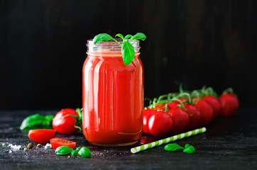 Organic fresh tomato juice in a glass jar, basil, cherry, salt, pepper and straw on dark black background. Clean eating and diet concept. Copy space