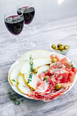 Appetizer for red wine prosciutto ham, slices of melon, olives and ciabatta bread with thyme