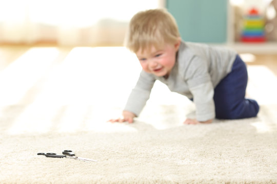 Baby in danger crawling towards a scissors