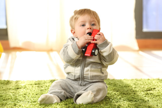 Baby sitting on a carpet biting a toy at home