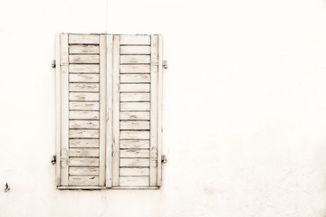 Rustic old grungy and weathered white grey wooden closed window shutters with peeling paint on a...