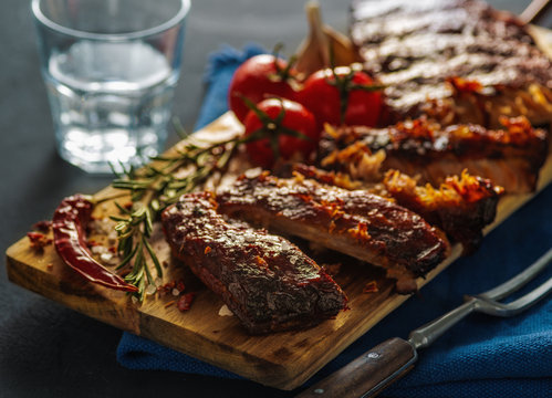 Delicious barbecued ribs seasoned with a spicy basting sauce and served with chopped fresh vegetables on an old rustic wooden chopping board in a country kitchen.