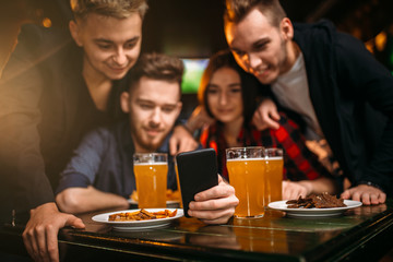 Fun company watches photo on phone in a sport bar