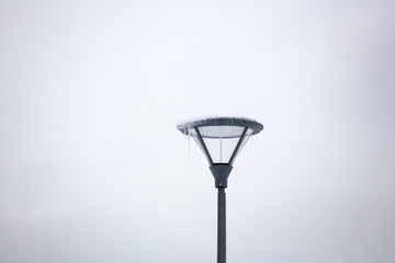LED street light with grey pole and armature aigainst white winter sky.