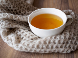 Eine Tasse Tee mit einem Wollschal auf einem braunen Holztisch, Lifestyle