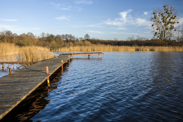 Long wooden jetty, lake with dry grasses on the shore - an autumn view