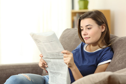 Serious teenager reading a newspaper at home