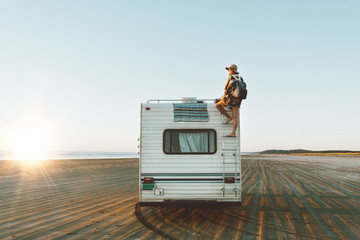 Charming girl with beautiful smile with hat, sunglasses, backpack climing on recreational vehicle...