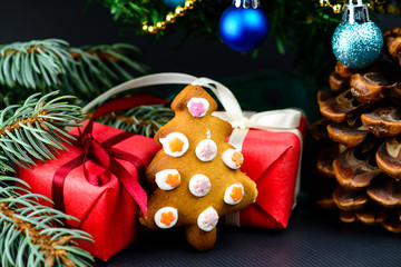 Gingerbread cookies in the shape of fir tree, pine cone, gifts wrapped in a red paper with white ribbon under decorated Christmas tree. Concept of Merry Christmas and New Year - Powered by Adobe