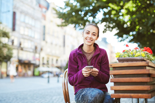 a young smiling woman tourist in sportswear seets on the bench in the center of Prague with a phone in the hands of. travel guide, tourism in Europe, woman tourist with smartphone on the street