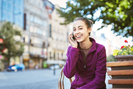 a young smiling woman tourist in sportswear seets on the bench in the center of Prague with a phone in the hands of. travel guide, tourism in Europe, woman tourist with smartphone on the street