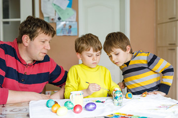 Two little kid boys and father coloring eggs for Easter holiday in domestic kitchen