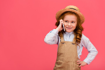 portrait of little smiling child talking on smartphone isolated on pink