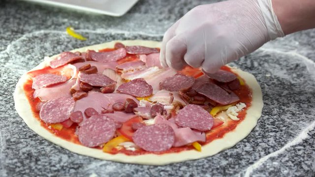 Chef making pizza, salami. Thin crust, vegetables and sausage.