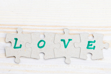 Word Love made of four pieces of jigsaw puzzle on light wooden table, close-up