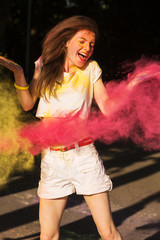 Cheerful brunette woman posing in a cloud of pink dry paint Holi at the park