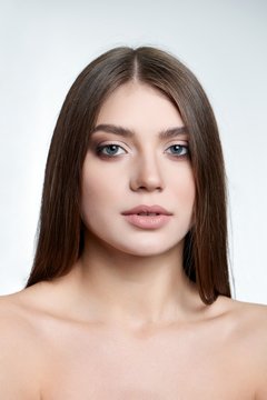 Fullface enface type of portrait of a beautiful green-eyed brunette with make-up on wearinf nude lipstick, light brown eyeshadows and mascara. Model is isolated on a white background in a photo studio