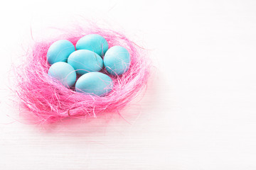 Easter eggs in a pink nest. Blue or turquoise chicken eggs on white wooden background