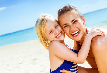 smiling healthy mother and daughter on seashore embracing