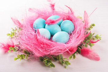 Easter eggs in a pink nest. Blue or turquoise chicken eggs on white wooden background. Pink feather, green plant