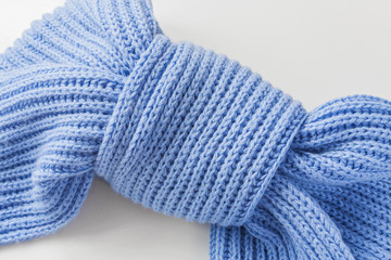 Light blue knitted scarf on a light background. Knot of a scarf in the form of a butterfly. Closeup