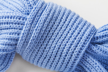 Light blue knitted scarf on a light background. Knot of a scarf in the form of a butterfly. Closeup