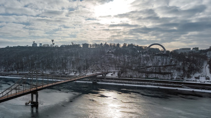 Aerial top view of pedestrian Park bridge in winter and Dnieper river from above, snow Kyiv cityscape, city of Kiev skyline, Ukraine
