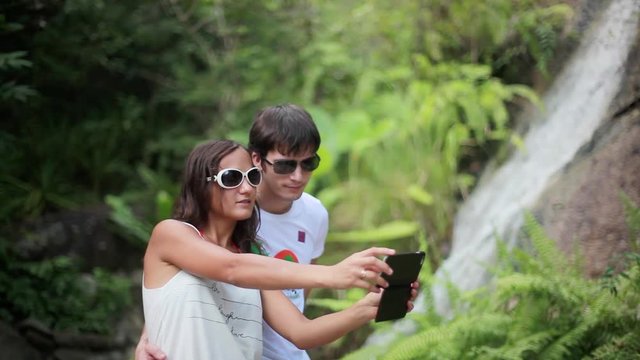 Happy couple wearing sunglasses taking selfie photo with beautiful waterfall background. 1920x1080