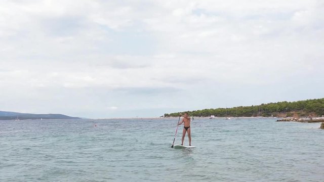 Adult man floats with the surfboard near to the beach
