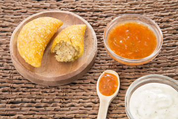 Colombian empanada with spicy sauce on wooden background