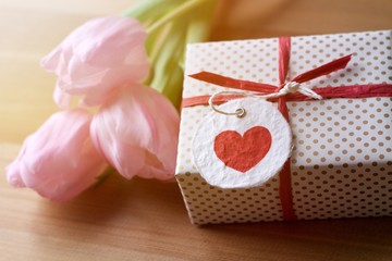 Geschenk mit Herz und rosa Tulpen im Sonnenlicht