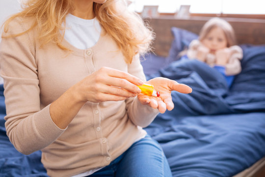 Medication. Mother holding a yellow medication and having red pills in her hand while her daughter lying in bed