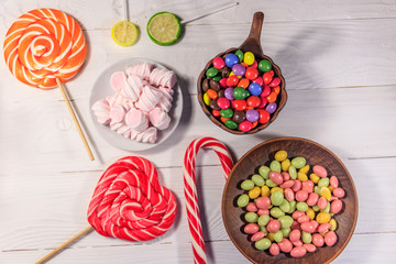 Colorful chocolate candies, lollipops, candy cane and marshmallows on wooden table