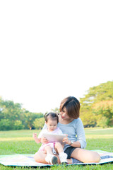 Mother and daughter outdoors in a meadow playing tablet. Mother with her daughter lying on grass and using digital tablet together. Mother and daughter education concept.
