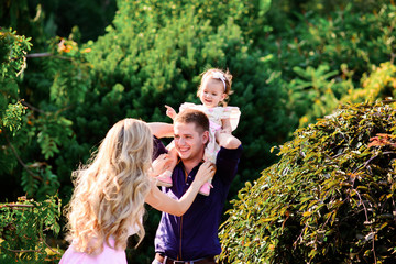 young happy family with little beautiful baby with blue eyes walking in summer park at sunset